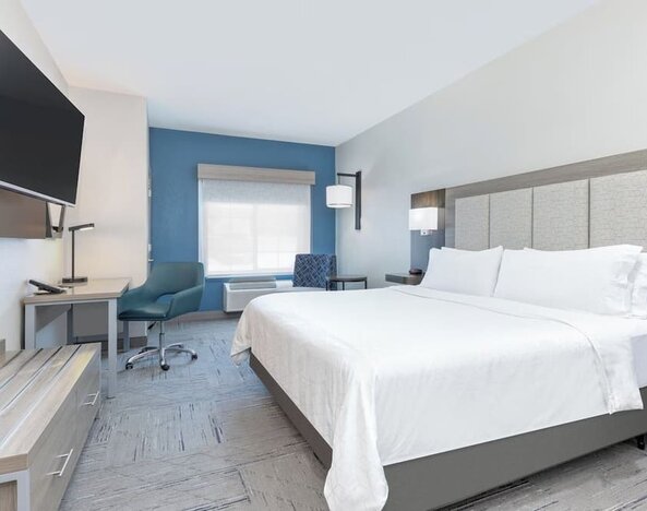 King guest room with a large bed, white bedding, blue accent wall, desk, armchair, and wall-mounted TV at Holiday Inn Express & Suites Granbury.