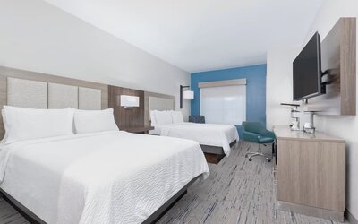 Guest room with two queen beds, white bedding, a wood-paneled headboard, blue accent wall, desk, armchair, and wall-mounted TV at Holiday Inn Express & Suites Granbury.