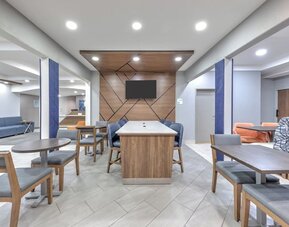 Hotel lobby with modern seating, tables, blue accent columns, wood paneling, and a wall-mounted TV at Holiday Inn Express & Suites Granbury.