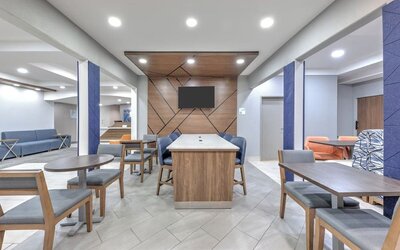Hotel lobby with modern seating, tables, blue accent columns, wood paneling, and a wall-mounted TV at Holiday Inn Express & Suites Granbury.