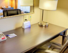 In-room workspace featuring a wooden desk, office chair, lamp, telephone, and wall mirror at Holiday Inn Express & Suites Granbury.