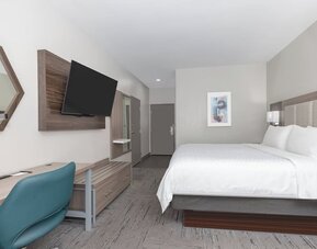 Spacious king guest room with a large bed, white bedding, wood furnishings, desk, blue office chair, and wall-mounted TV at Holiday Inn Express & Suites Granbury.