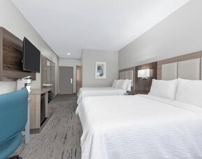 Guest room with two queen beds, white bedding, wood headboard, blue office chair, desk, dresser, and wall-mounted TV at Holiday Inn Express & Suites Granbury.