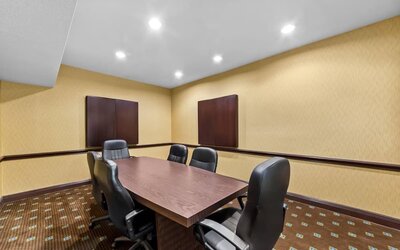 Private hotel meeting room with a large rectangular conference table, six black leather office chairs, warm neutral walls, recessed lighting, and wall-mounted decorative panels.