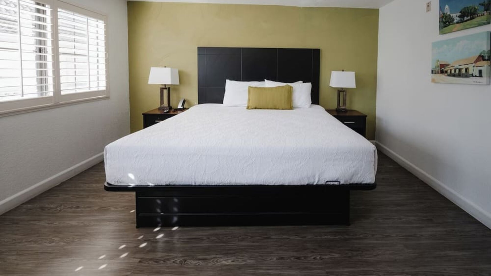 Bright king guest room with a large bed, white bedding, green accent wall, bedside tables, desk, and windows with natural light at Western Inn.