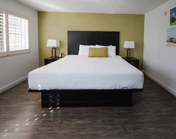 Bright king guest room with a large bed, white bedding, green accent wall, bedside tables, desk, and windows with natural light at Western Inn.