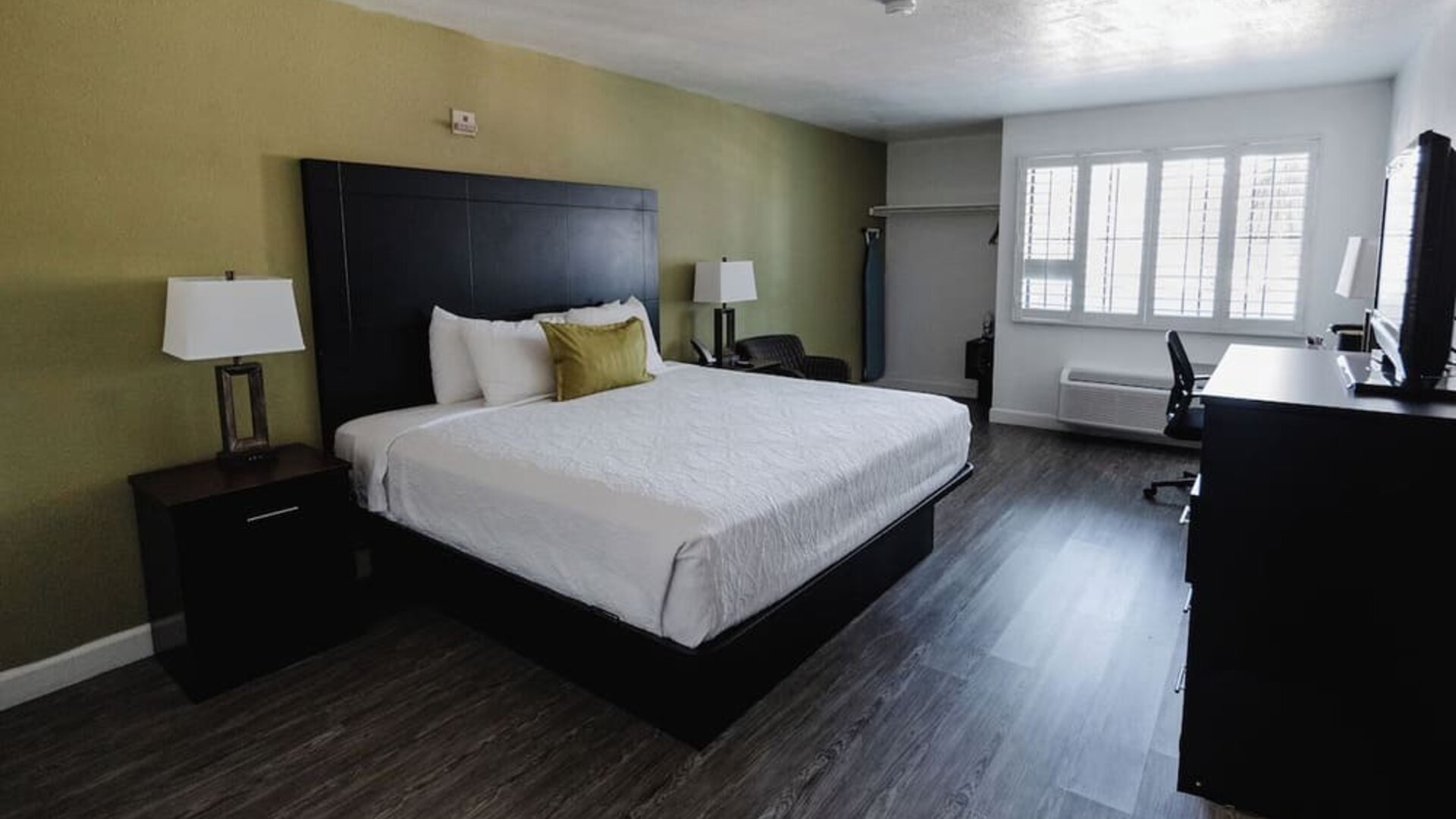 King guest room featuring a king bed, white bedding, green accent wall, bedside tables and lamps, desk, and large windows at Western Inn.