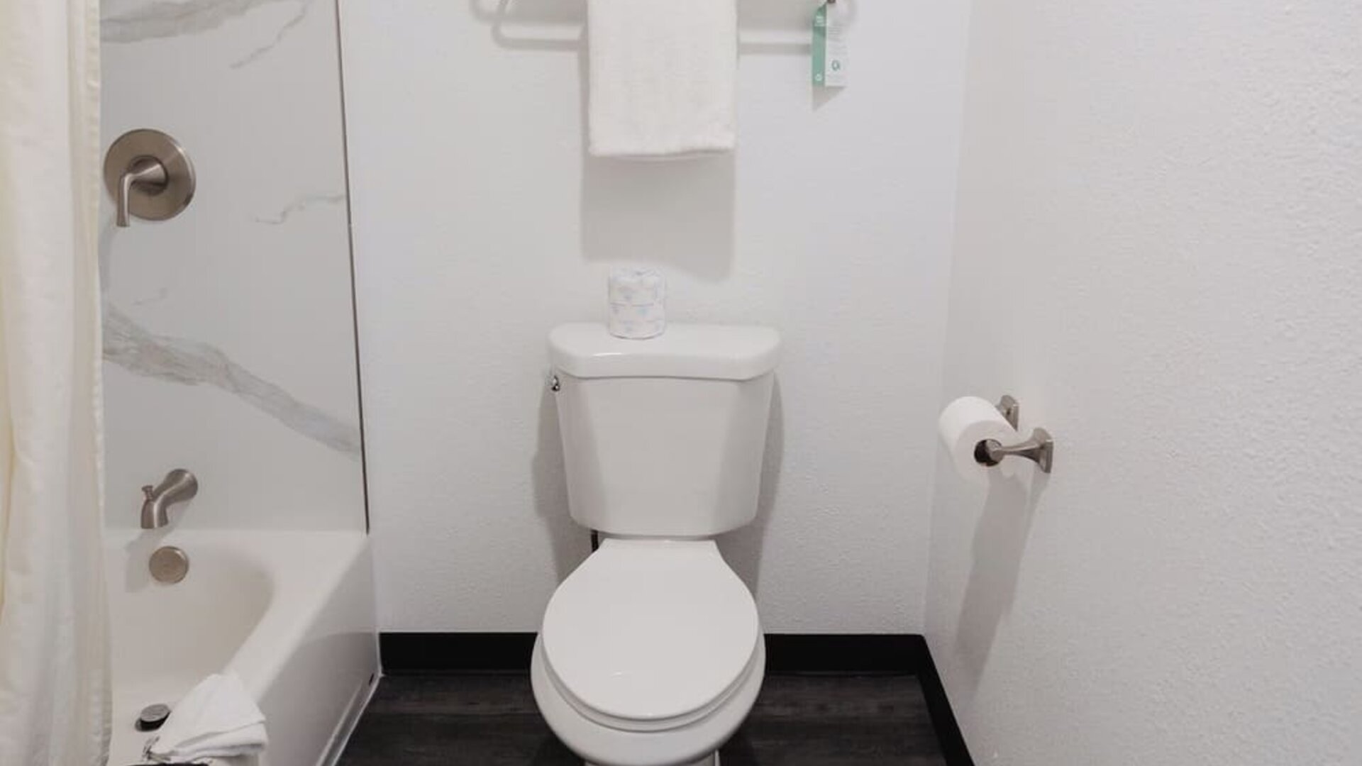 Bathroom with a bathtub/shower combination, white tile surround, towel rack, and toilet at Western Inn.