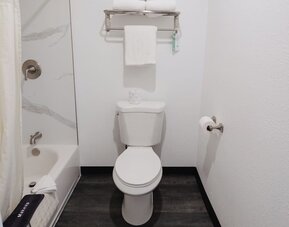 Bathroom with a bathtub/shower combination, white tile surround, towel rack, and toilet at Western Inn.