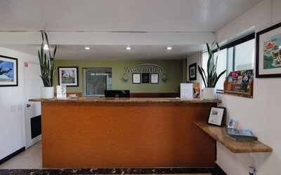 Reception desk with wooden counter, Western Inn signage, decorative plants, framed artwork, and guest information materials at Western Inn.