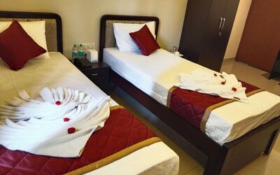 Twin bed guest room featuring white bedding, burgundy accent pillows, quilted runners, decorative folded towels with red flowers, and a bedside table with a telephone.