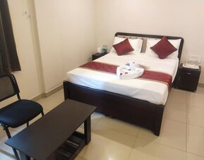 Comfortable double bed guest room featuring white linens, burgundy decorative pillows, matching bed runner, folded towels, bedside cabinets, and a seating area.