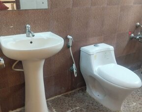 Private hotel bathroom featuring a white pedestal sink, modern toilet, handheld bidet sprayer, wall-mounted shower fixtures, large mirror, and patterned tile flooring.