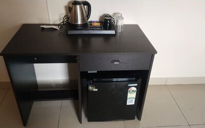 Black wooden refreshment station at The Nisarga Suites featuring an electric kettle, mugs, drinking glasses, beverage supplies, and a mini refrigerator.