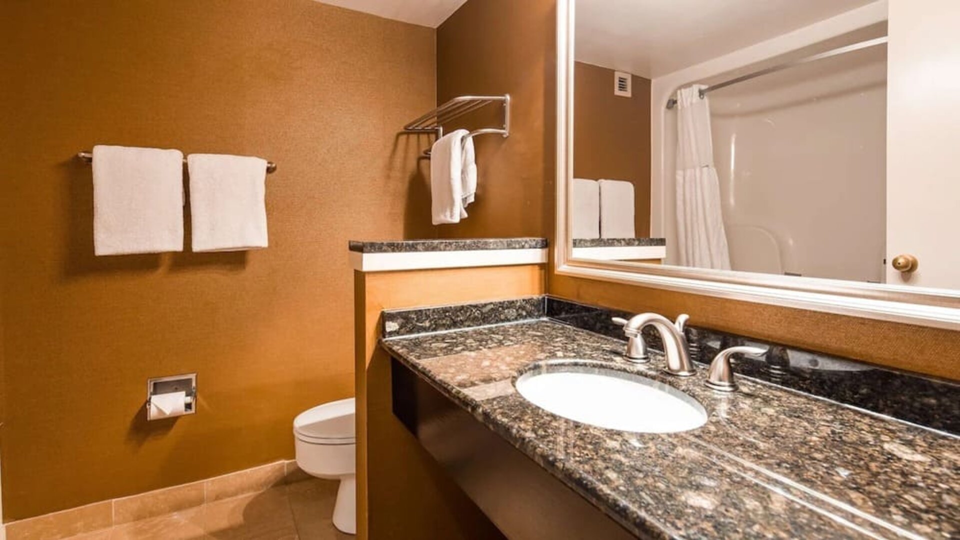 Bathroom vanity with a granite countertop, oval sink, chrome fixtures, large mirror, brown walls, and white towels at Best Western Plus BWI Airport Arundel Mills.