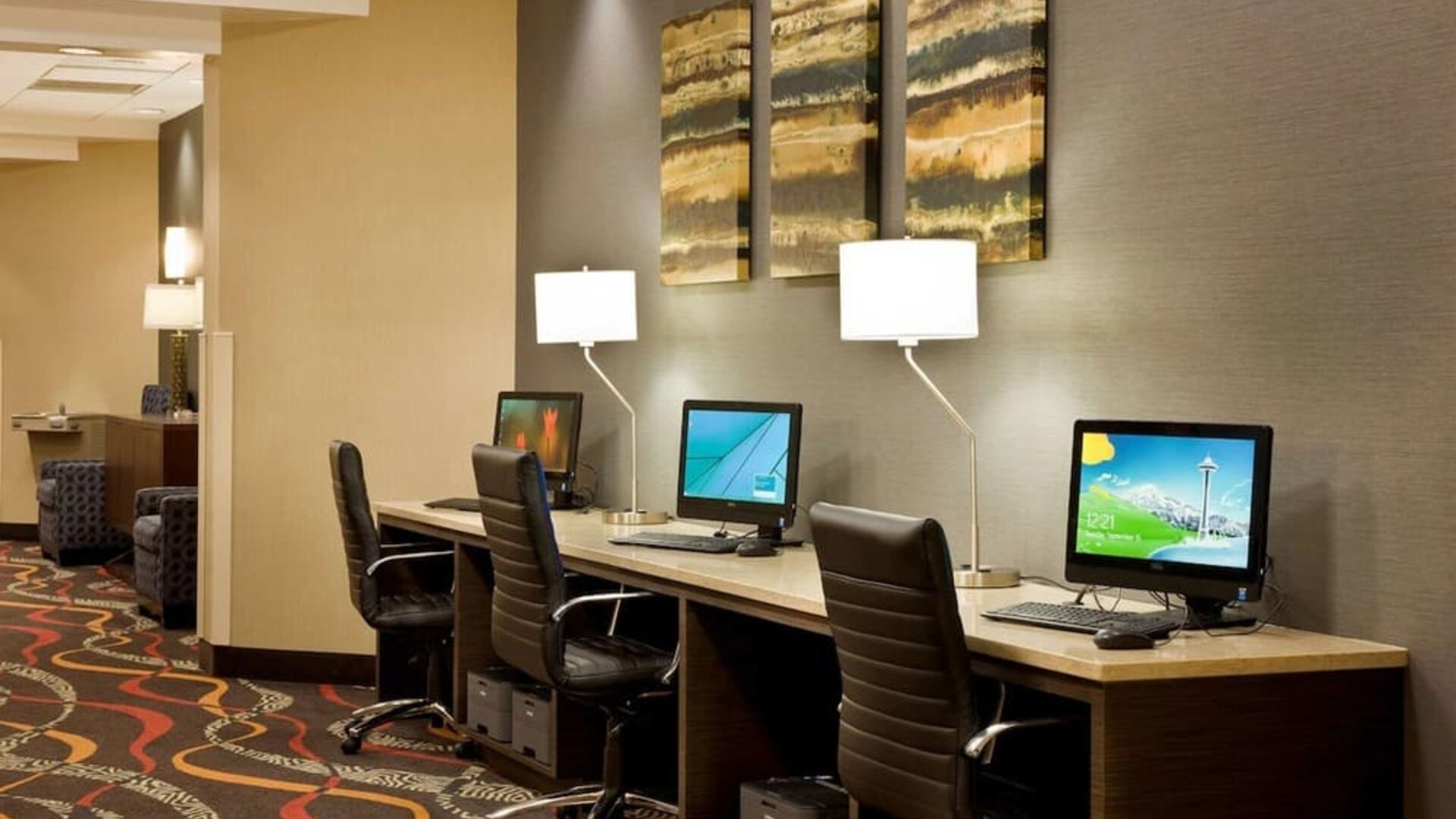 Business center featuring multiple computer workstations, office chairs, desk lamps, and wall art at Best Western Plus BWI Airport Arundel Mills.