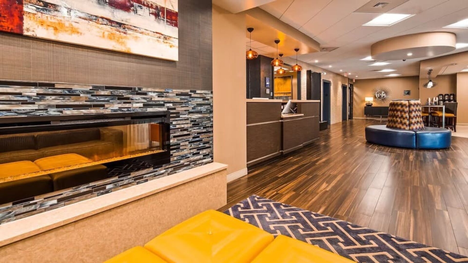 Hotel reception area with a front desk, modern wood finishes, decorative pendant lighting, patterned wall accents, and guest seating at Best Western Plus BWI Airport Arundel Mills.