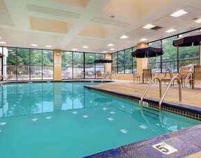 Indoor swimming pool with clear turquoise water, surrounding deck, metal handrails, large windows, and outdoor greenery visible through the glass at Best Western Plus BWI Airport Arundel Mills.