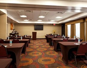 Meeting area arranged with tables and chairs, water bottles, a presentation screen, a podium, and large curtained windows at Best Western Plus BWI Airport Arundel Mills.