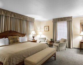 Spacious king guest room with a large wooden bed, beige bedding, upholstered seating, a round coffee table, framed artwork, and a separate desk area at Liberty Hotel Cleburne, an Ascend Hotel Collection Member.