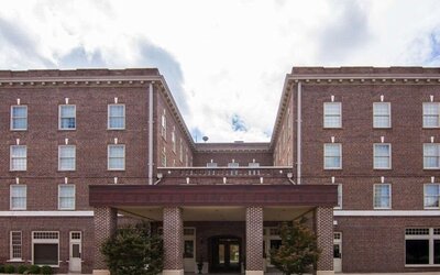 Exterior view of Liberty Hotel Cleburne, showcasing its multi-story red-brick architecture, symmetrical windows, covered main entrance, and landscaped frontage.