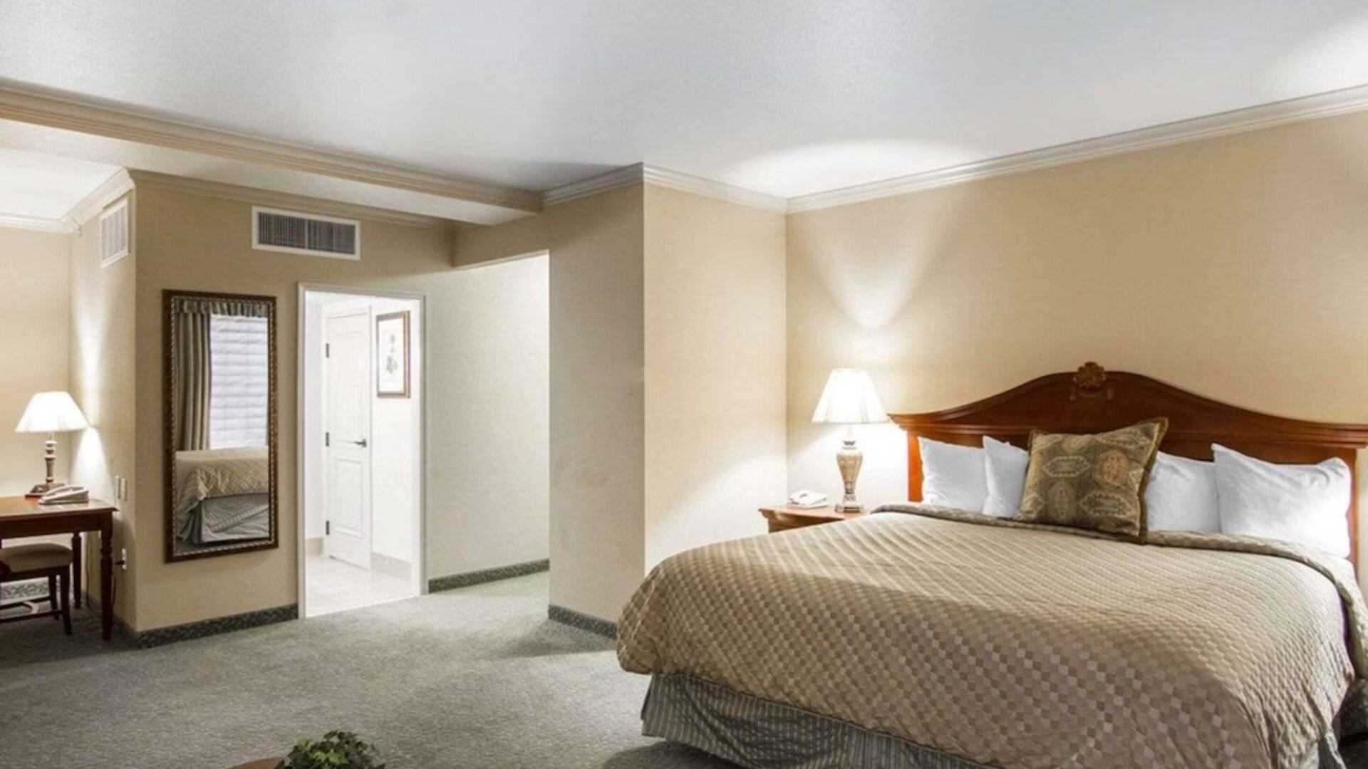 ing bedroom featuring a traditional wooden bed frame, beige patterned bedding, white pillows, bedside lamps, neutral decor, and carpeted flooring at Liberty Hotel Cleburne, an Ascend Hotel Collection Member.