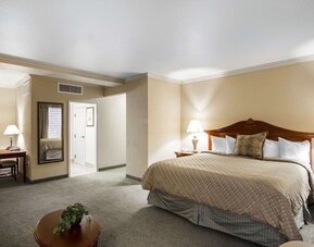 ing bedroom featuring a traditional wooden bed frame, beige patterned bedding, white pillows, bedside lamps, neutral decor, and carpeted flooring at Liberty Hotel Cleburne, an Ascend Hotel Collection Member.