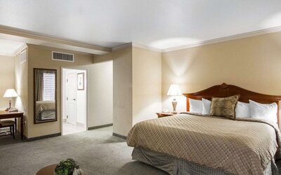 ing bedroom featuring a traditional wooden bed frame, beige patterned bedding, white pillows, bedside lamps, neutral decor, and carpeted flooring at Liberty Hotel Cleburne, an Ascend Hotel Collection Member.