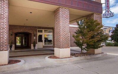Exterior entrance of Liberty Hotel Cleburne, featuring a red-brick facade, covered porte-cochère, brick columns, landscaped planters, and the hotel's vertical sign.