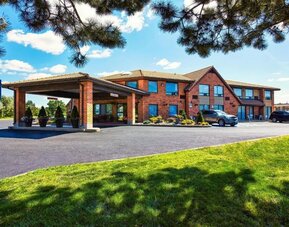 Exterior view of Comfort Inn Alma, showcasing its red-brick facade, covered entrance, blue hotel signage, parking area, and landscaped lawn.