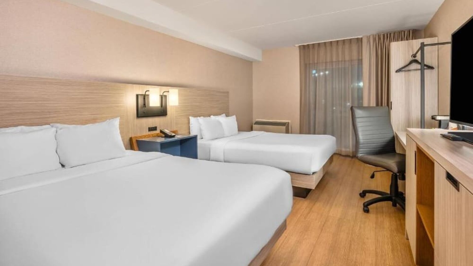 Guest room with two beds, crisp white bedding, a shared blue bedside table, modern wall sconces, a light wood headboard, and contemporary decor at Comfort Inn Alma.