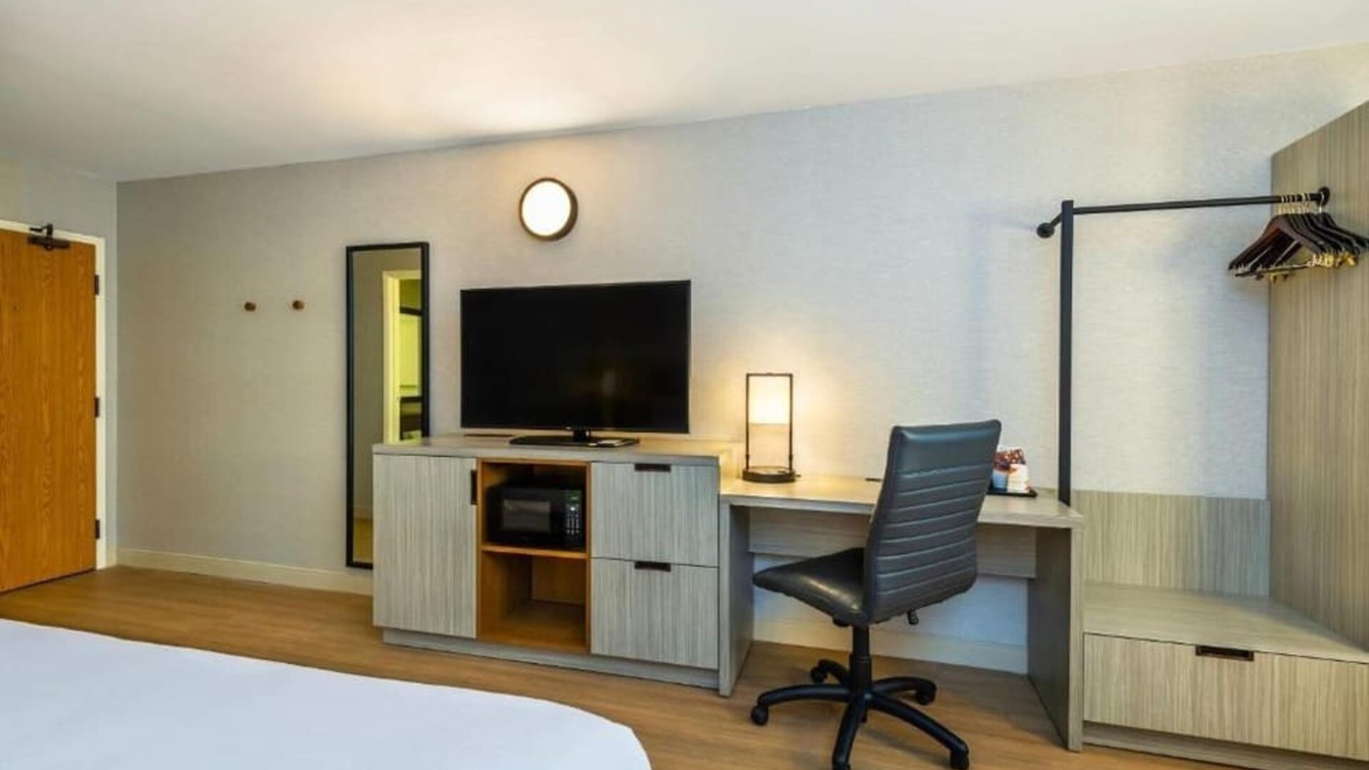 In-room workspace featuring a desk, ergonomic office chair, flat-screen television, microwave, dresser, and open clothing rack in a contemporary guest room at Comfort Inn Alma.
