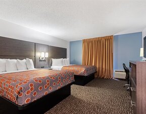 Guest room featuring two beds with orange geometric-patterned bedspreads, white pillows, a dark wood headboard, blue accent walls, and contemporary furnishings at Chicago Club Inn & Suites.