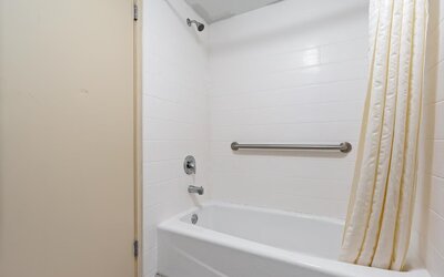 Bathroom featuring a white bathtub and shower curtain, white tiled walls, chrome shower fixtures, and a horizontal stainless-steel grab bar at Chicago Club Inn & Suites.