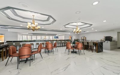Hotel dining and breakfast area with marble-patterned flooring, orange upholstered chairs, tables, a breakfast counter, and beverage stations at Chicago Club Inn & Suites.