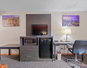 In-room workspace featuring a desk and office chair, flat-screen television, microwave, mini refrigerator, telephone, and wall-mounted artwork in a guest room at Chicago Club Inn & Suites.