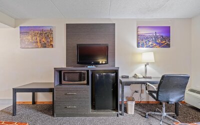 In-room workspace featuring a desk and office chair, flat-screen television, microwave, mini refrigerator, telephone, and wall-mounted artwork in a guest room at Chicago Club Inn & Suites.