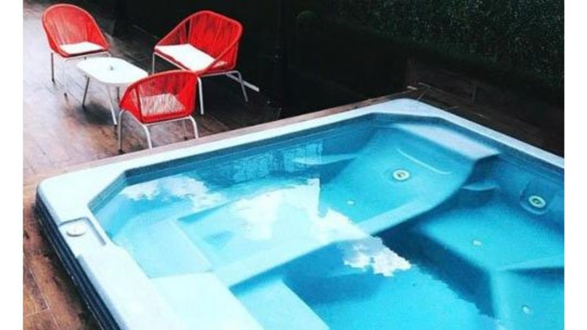 An outdoor swimming pool with built-in seating and clear blue water, surrounded by a wooden deck and red outdoor chairs at Residencial & Hotel Palazzo.