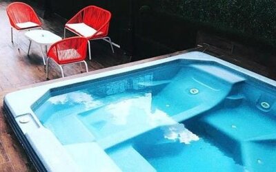 An outdoor swimming pool with built-in seating and clear blue water, surrounded by a wooden deck and red outdoor chairs at Residencial & Hotel Palazzo.
