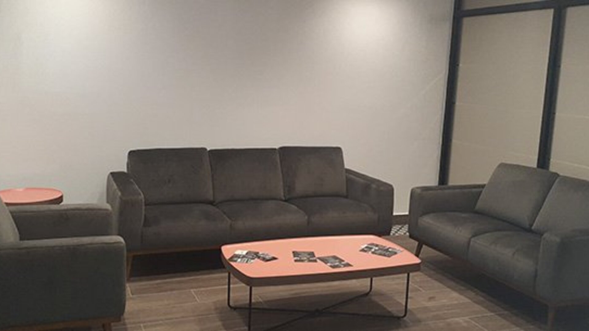 A lounge with dark upholstered sofas and armchairs arranged around a coral-coloured coffee table in a room with tiled flooring at Residencial & Hotel Palazzo.