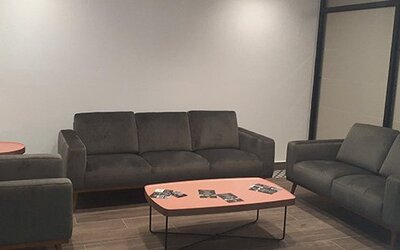 A lounge with dark upholstered sofas and armchairs arranged around a coral-coloured coffee table in a room with tiled flooring at Residencial & Hotel Palazzo.