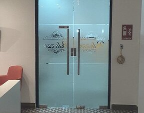 A reception area with frosted glass double doors, a wall-mounted television, coral chairs and a dark countertop at Residencial & Hotel Palazzo.