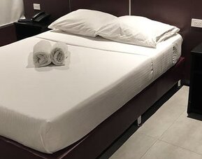 A double bed with white linens and rolled towels, dark bedside tables and wood-look flooring at Residencial & Hotel Palazzo.