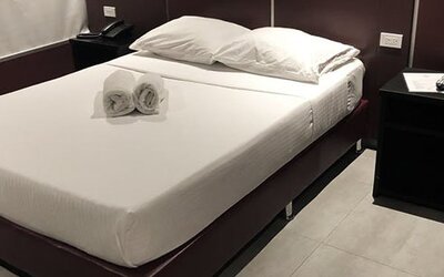 A double bed with white linens and rolled towels, dark bedside tables and wood-look flooring at Residencial & Hotel Palazzo.