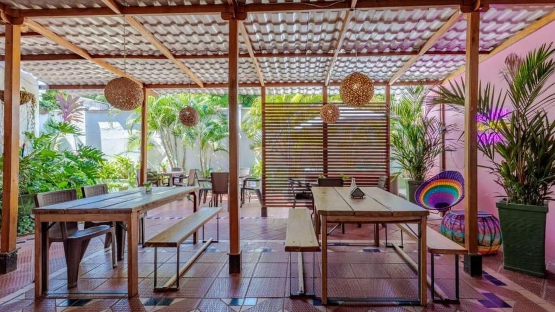 A covered outdoor dining area with wooden tables and benches, woven pendant lights, tropical plants and colourful decorative accents at Mucura Hotel And Spa.