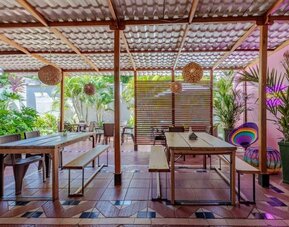 A covered outdoor dining area with wooden tables and benches, woven pendant lights, tropical plants and colourful decorative accents at Mucura Hotel And Spa.