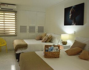 A twin-bedroom setup with two beds dressed in white linens and beige throws, decorative cushions, a yellow accent chair, built-in wardrobes and a wall-mounted air conditioner at Mucura Hotel And Spa.
