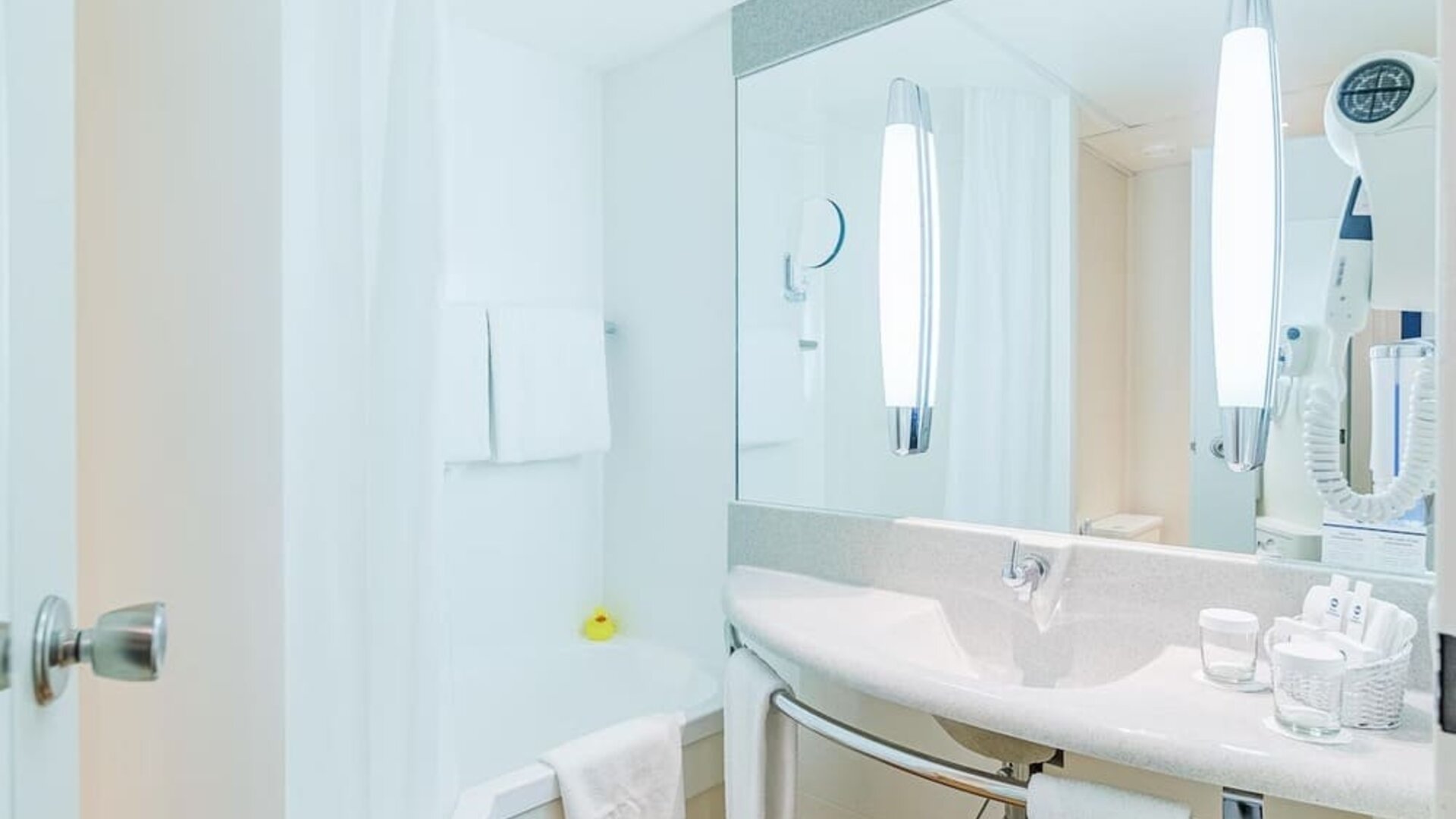A bright, modern hotel bathroom with a bathtub and shower, a wide vanity basin, a large mirror, wall-mounted lighting, fresh towels and complimentary toiletries at Best Western Macrander Hotel Frankfurt/Kaiserlei.