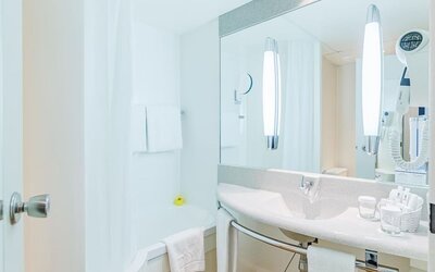 A bright, modern hotel bathroom with a bathtub and shower, a wide vanity basin, a large mirror, wall-mounted lighting, fresh towels and complimentary toiletries at Best Western Macrander Hotel Frankfurt/Kaiserlei.