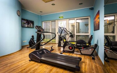 The hotel's fitness room, equipped with treadmills, stationary exercise bikes and other cardio equipment, with mirrored walls, blue accents and wood-effect flooring at Best Western Macrander Hotel Frankfurt/Kaiserlei.